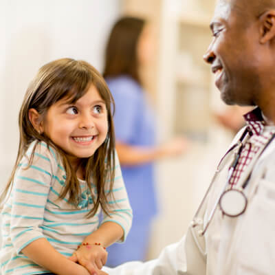 Little girl giving a doctor an adorable smile, her shoulders are scrunched and hands are together