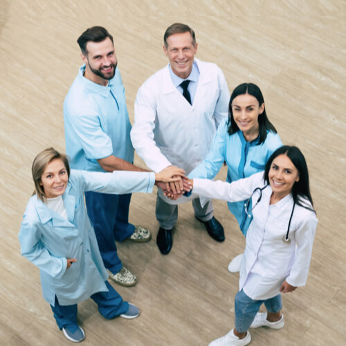 Looking down on a team of caregivers in a circle with their hands together, smiling at the camera